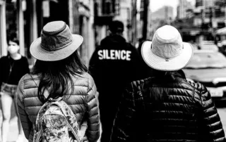 Two ladies wearing Tilley hats balance the inscription "Silence" in an interesting way on a street in Toronto, Canada. Picture by Maksim Sokolov (maxergon.com); Wikimedia Commons
